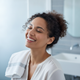 Portrait of a smiling woman in her 30s, looking happy and content against a blurred background.